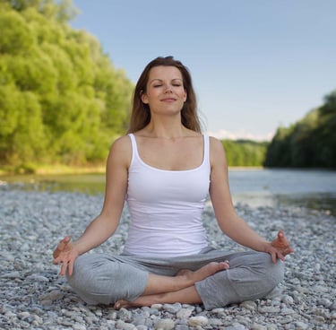 A woman on a lotus pose, sitting by the lake on a bedrock.