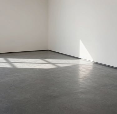 A minimalist, high-angle photograph of an empty gallery space in a North American / US museum. Soft light spills onto a polished grey floor, casting long shadows. The palette is dominated by off-white and charcoal grey, reflecting a contemporary and professional atmosphere.