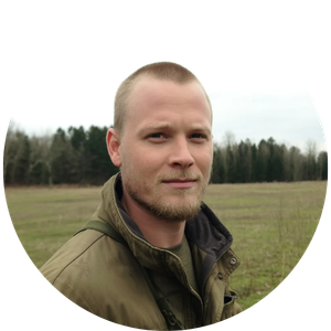 A man with a short beard and military jacket standing in an open field.