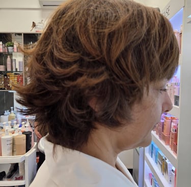 Side profile of a woman with a layered, honey-brown shag haircut and flipped ends in a professional hair salon.