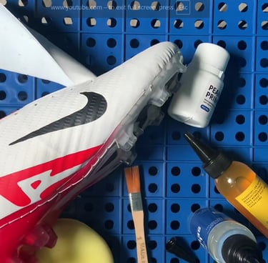 White and red Nike soccer cleat being repaired with shoe glue, primer, and brushes on a blue pegboard.
