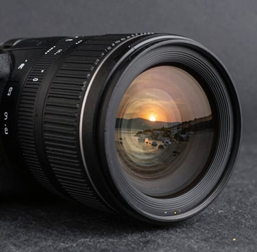 A professional camera lens reflecting the sunset of Bodrum, sharp focus, metallic textures, dark slate grey background.