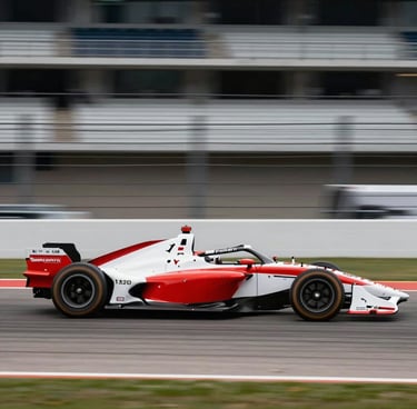 A side-profile panning shot of an IndyCar with red and white livery speeding across a North American / US racetrack. The background is a motion blur of gray asphalt and grandstands, emphasizing raw velocity and precision.