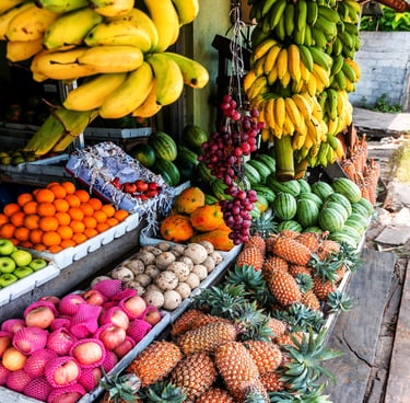 A vibrant market stall overflowing with tropical fruits, including yellow bananas, fresh pineapples, and green watermelons.
