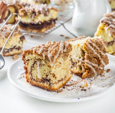 Slices of moist coffee cake with a cinnamon swirl and crumble topping, drizzled with white glaze on a plate.