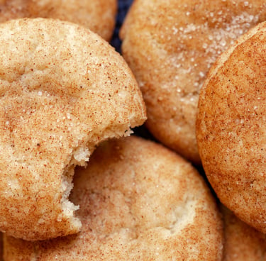 Close-up of golden snickerdoodle cookies coated in cinnamon sugar, with a bite taken out of one cookie.