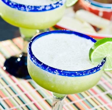 A classic lime margarita on ice in a salt-rimmed glass, garnished with a fresh lime wheel on a mat.