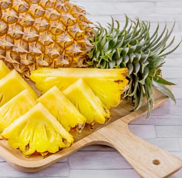 A whole fresh pineapple next to sweet, yellow sliced pineapple chunks on a wooden cutting board.