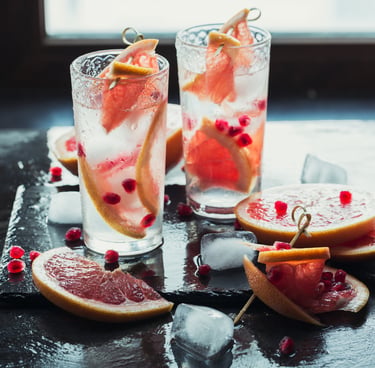 Two tall glasses of sparkling grapefruit drinks with ice, garnished with fresh grapefruit slices and pomegranate seeds.