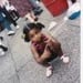 A young girl with pigtails crouching on a sidewalk outdoors in a public area.