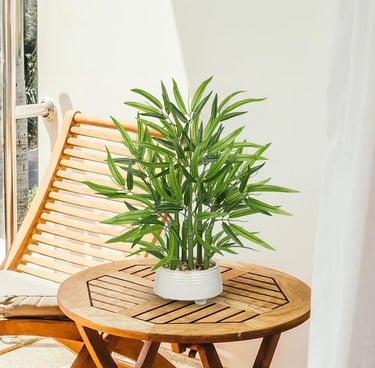 Artificial bamboo plant in a white ceramic pot on a wooden patio table.
