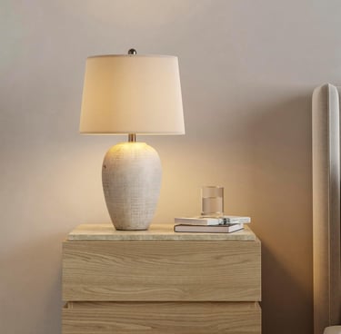 Ceramic table lamp with textured base on a light wood nightstand in a neutral bedroom.