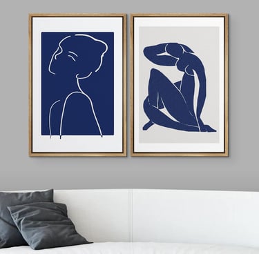 Set of two minimalist navy blue female figure line art prints in oak frames above a white sofa.