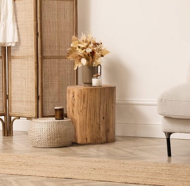 Boho living room decor featuring a natural wood stump side table, dried flowers, and a woven floor pouf.