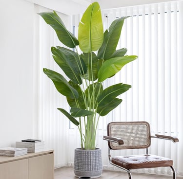 Large artificial bird of paradise plant in a grey pot next to a modern leather chair.