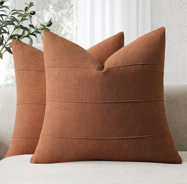 Set of two terracotta orange textured throw pillows with horizontal stripe detailing on a neutral sofa.