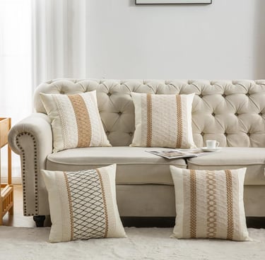Set of four bohemian cream throw pillows with woven brown patterns on a tufted beige sofa.