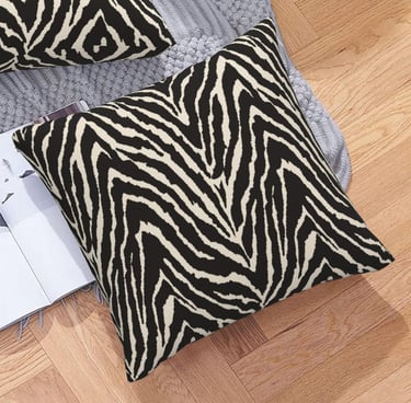 Black and white zebra print decorative throw pillow on a grey rug and wooden floor.