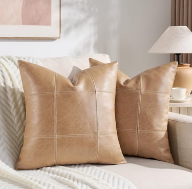 Two tan faux leather decorative throw pillows with a modern grid pattern on a white living room sofa.