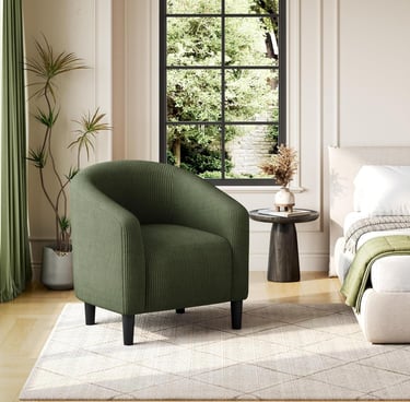 Modern green corduroy barrel chair in a bright bedroom sitting on a diamond pattern rug.