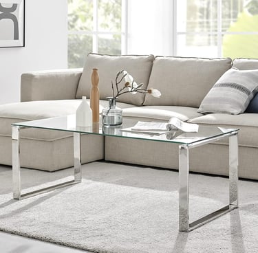 Modern rectangular glass coffee table with chrome legs in a bright living room setup.