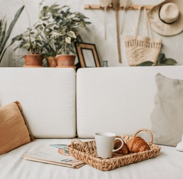 Cream linen sofa with woven pillow, styled with potted plants, coffee mug and woven tray