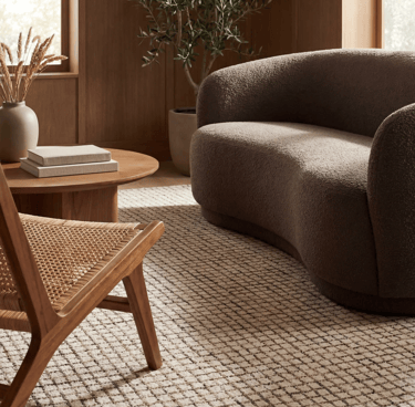 Modern living room with a brown boucle loveseat, woven rattan chair, and neutral grid area rug.