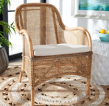 Woven rattan armchair with a white cushion on a round jute rug in a bright living room.