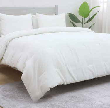 Plush white down alternative comforter set on a bed with matching pillows and a green plant.
