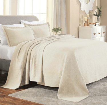 Elegant beige quilted coverlet set on a modern bed with matching pillow shams in a neutral bedroom.