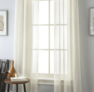 Elegant cream linen sheer curtains hanging on a dark rod over a bright window in a modern room.