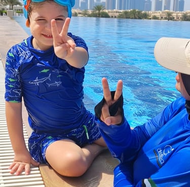 A smiling boy in blue swimwear by an infinity pool with the Dubai