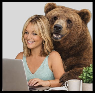 Smiling woman working on a laptop with a large brown grizzly bear looking over her shoulder.
