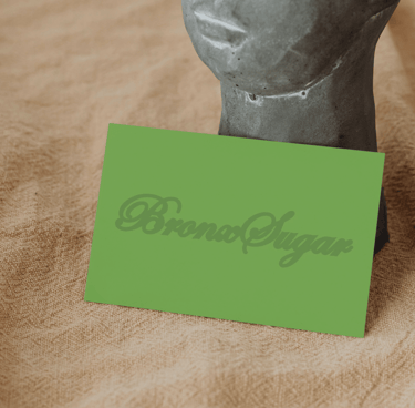 Green Bronx Sugar business card resting against a stone face statue on textured beige fabric.