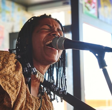 A soulful female singer with braided hair performing live into a microphone during a concert.