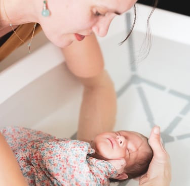 Bébé emmaillotté dans une couverture, dans les bras d'Audrey pendant le Bain des Merveilles