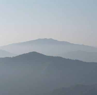 A minimalist wide-angle landscape photograph of misty mountains in the distance, featuring a soft grey and light blue color palette, clean composition, International / Western setting, high-end fine art style.