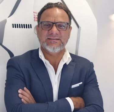 a man adnan sarfraz in a suit and glasses standing in front of a wall