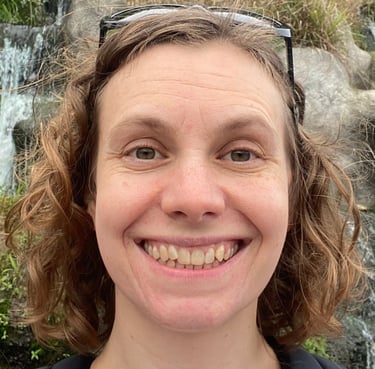 a woman with sunglasses and a backpack standing in front of a waterfall