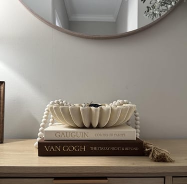 A decorative scalloped bowl and wooden prayer beads stacked on art coffee table books.