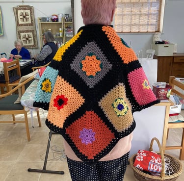 A brightly coloured women's crocheted shawl viewed from behind.