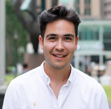 Smiling young professional man with dark hair wearing a white button-down shirt outdoors.