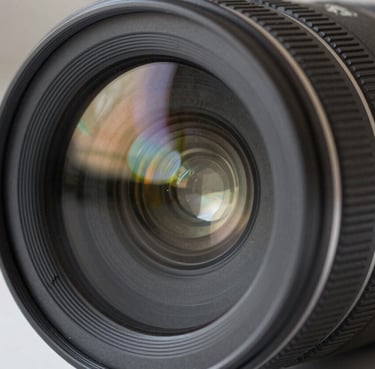 Close-up of a professional camera lens showing complex glass elements and multi-layered coatings, charcoal gray finish, sharp focus with soft bokeh, studio lighting in a North American setting.