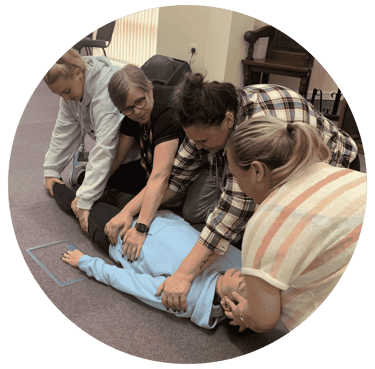 Four adults kneel around a person lying on the floor during a first aid training session