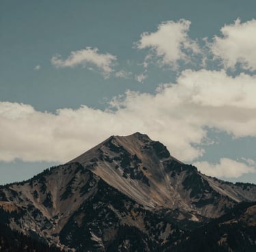 Minimalist wide shot of a solitary peak in the North American / US Cascades, surrounded by soft clouds, teal gray and off-white tones, calm and professional.