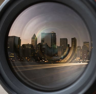 Extreme close-up of a camera lens reflecting a North American / US city skyline at twilight, muted champagne gold light trails, deep obsidian black glass.