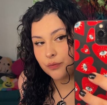 Mujer joven con cabello negro rizado y piercings faciales tomándose una selfie