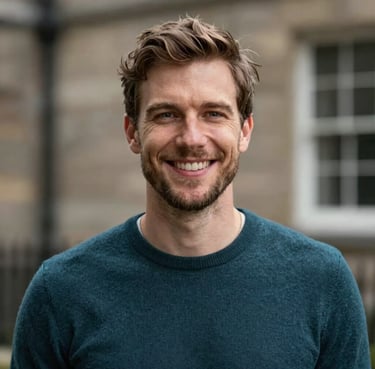 A portrait of a smiling British / UK travel creator in a smart-casual dark teal sweater.