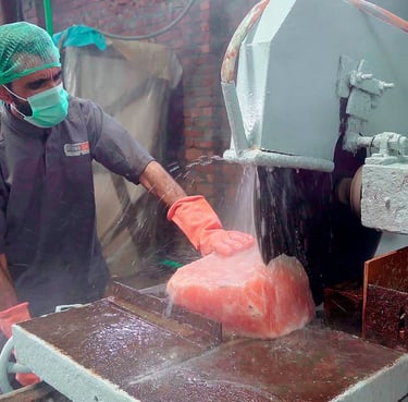 Worker cutting a large salt block with a machine in a factory, wearing safety gear and gloves.