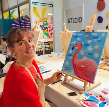 Une femme souriante peint un flamant rose sur une toile lors d’un atelier in strasbourg